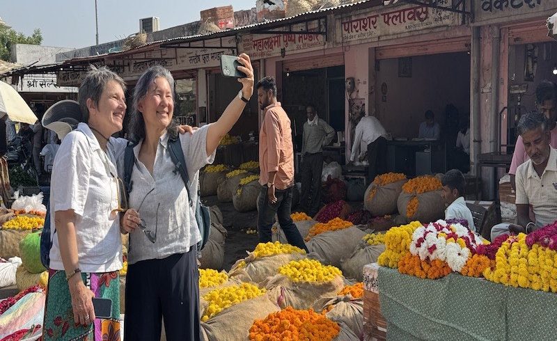Two travellers enjoying a cultural walking tour at Jaipur's colourful flower market, surrounded by traditional flower stalls and local vendors.